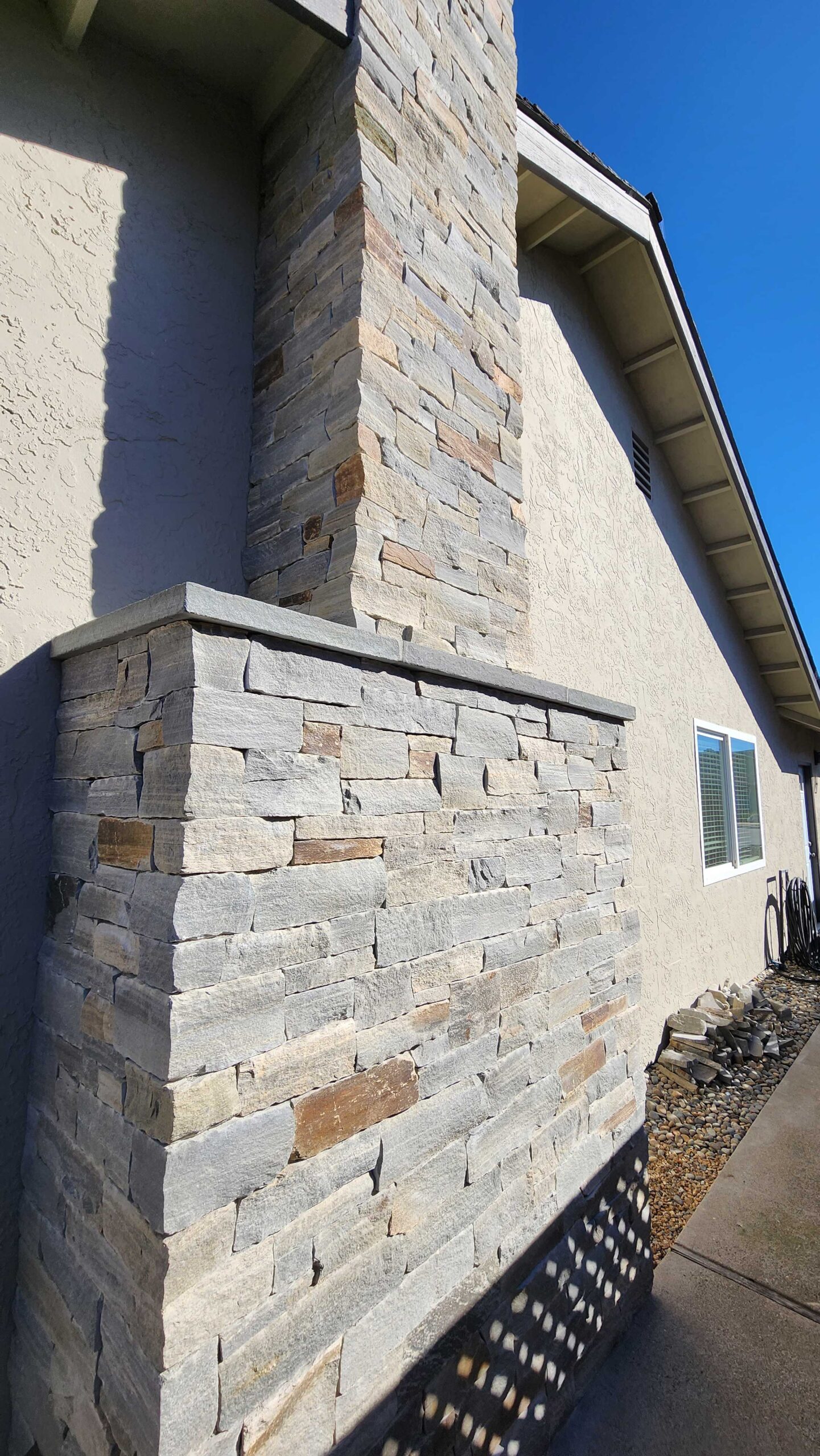 An exterior view of a light-colored stone chimney and base foundation work on a residential home, showing the contrast between the stone wor
