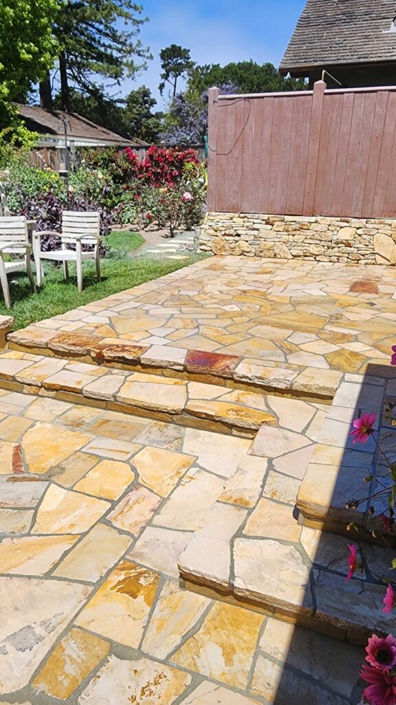 Flagstone patio with irregular tan and golden stone pavers in random pattern, showing completed work.