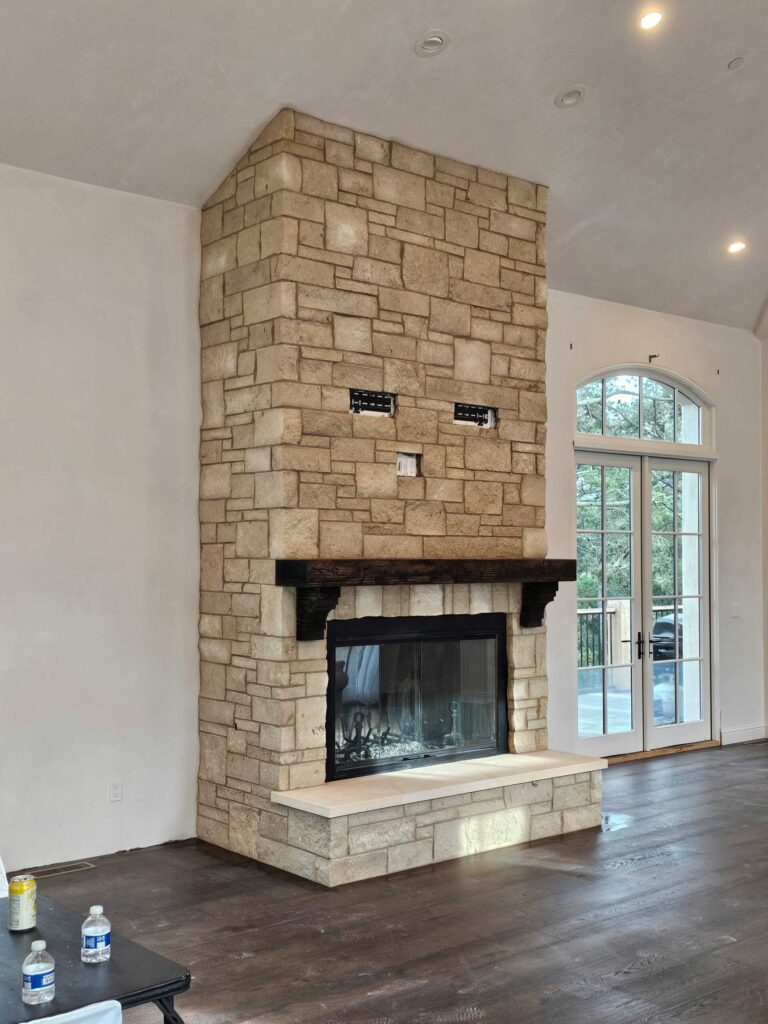 Interior masonry fireplace with tan stone chimney breast in running bond pattern and black metal firebox