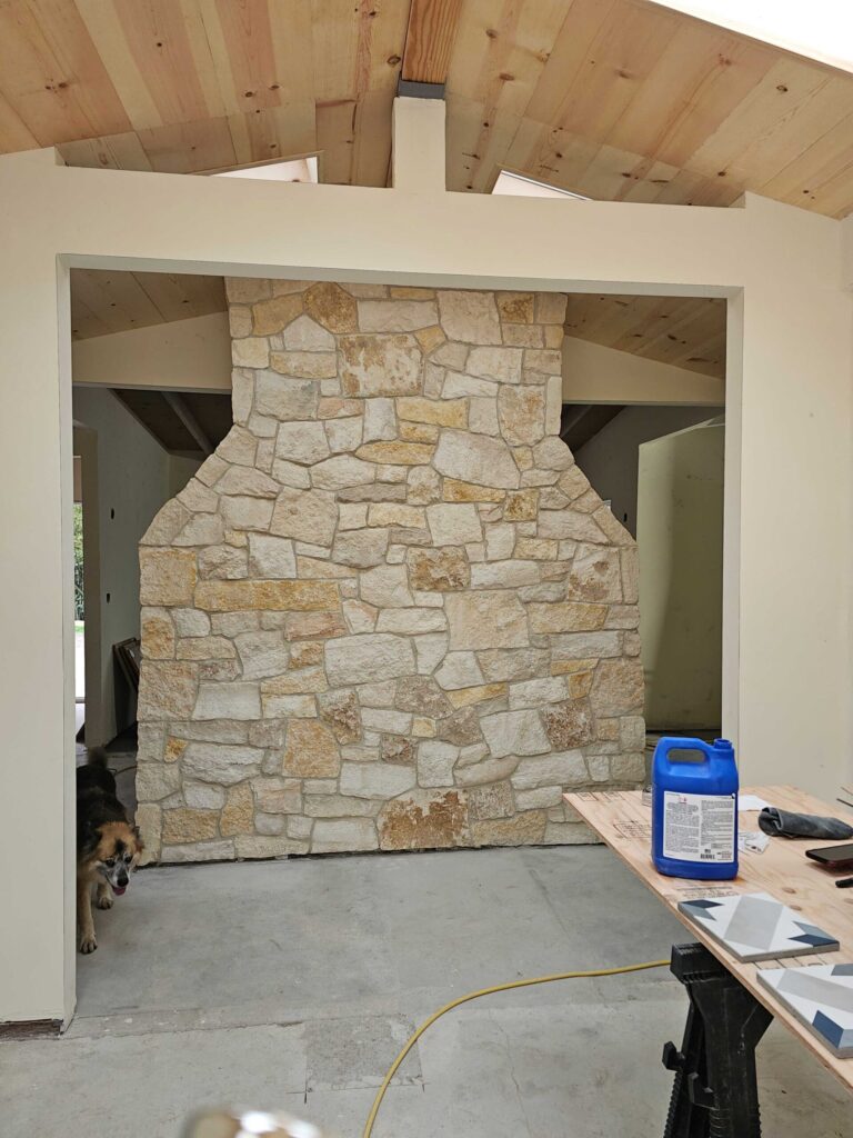 Masonry fireplace chimney under construction showing coursed stone veneer work in progress inside a residential room
