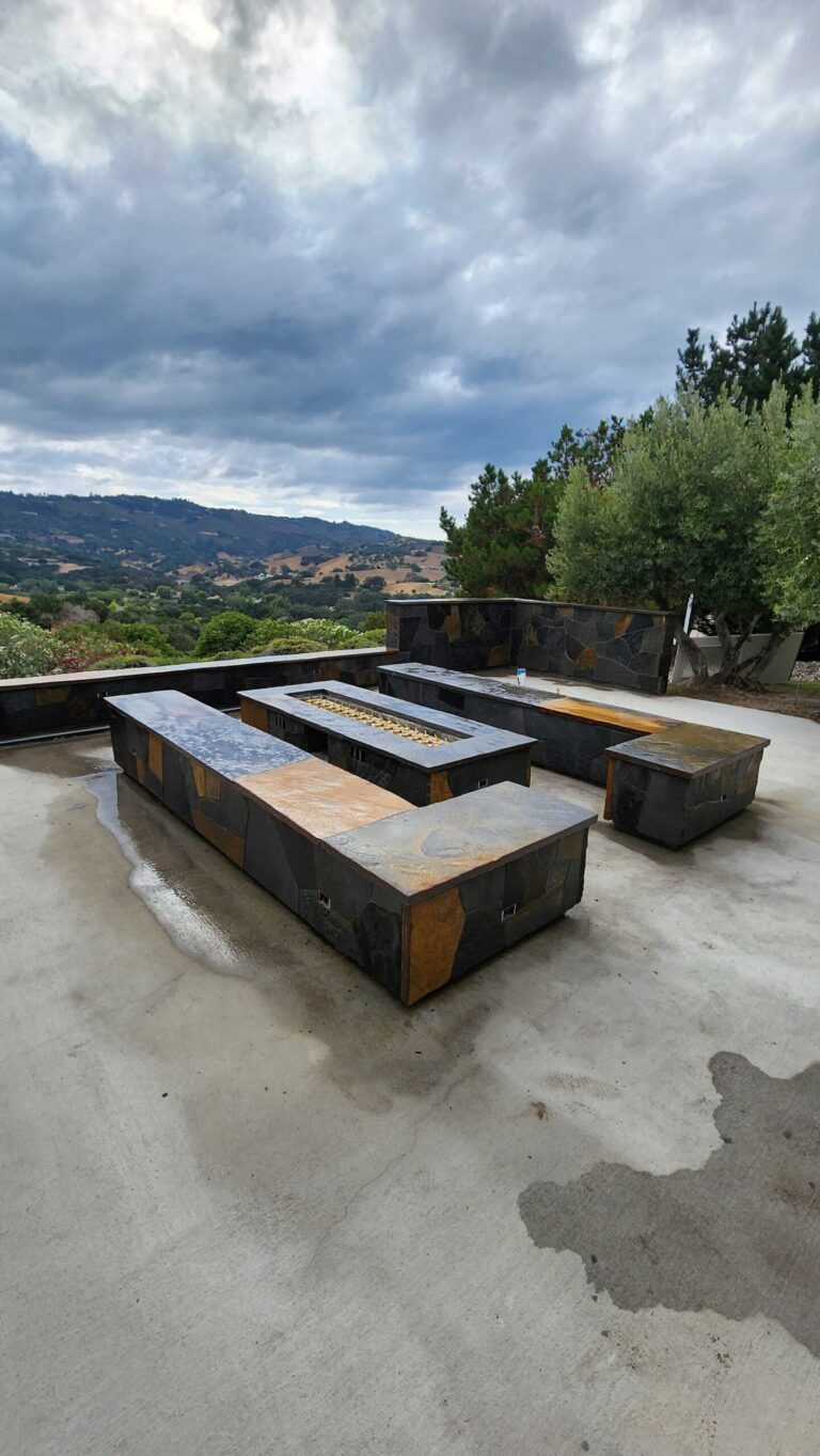 Custom concrete fire pit benches with metal frames on patio overlooking hillside landscape