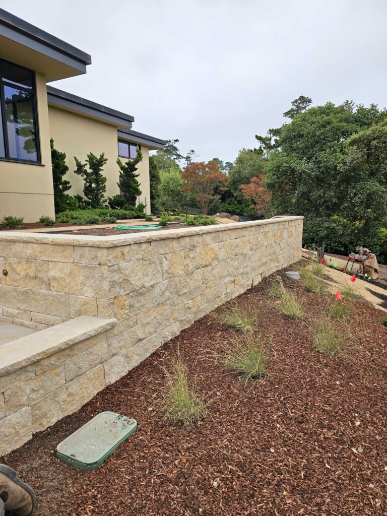 Completed residential made from stacked tan and beige stone blocks with landscaping.