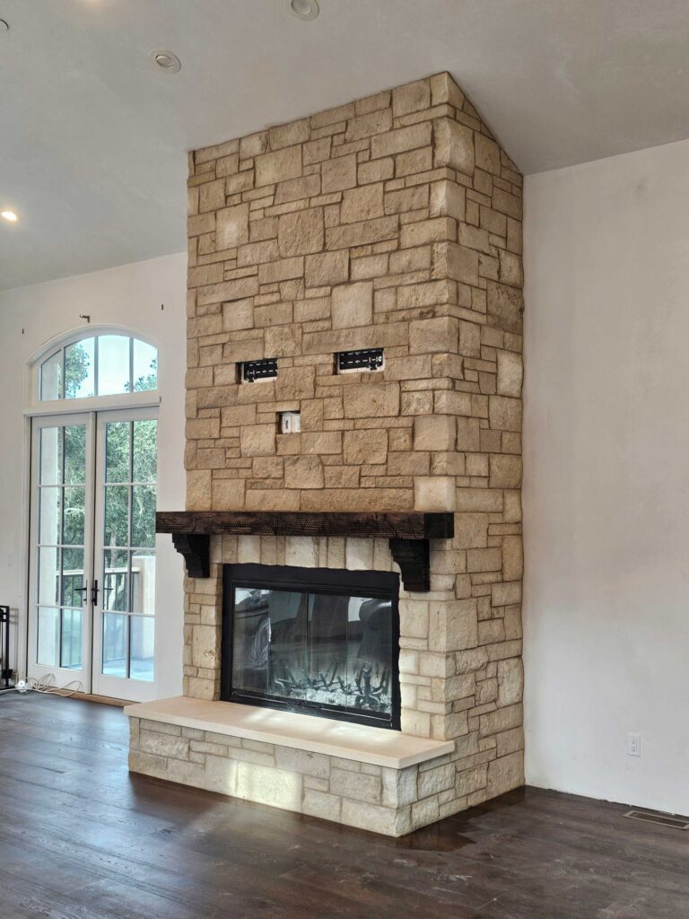 Interior stone fireplace with tan ashlar masonry construction, black metal firebox, and dark wood mantel.